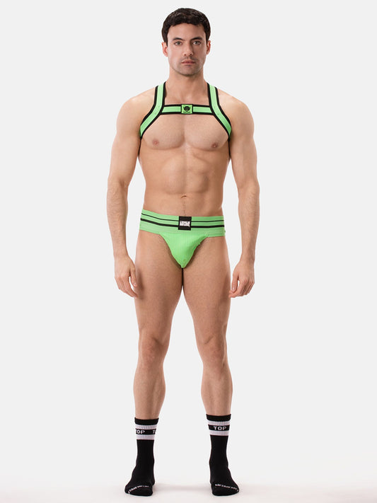 Man wearing a neon green party harness and jockstrap on a white background