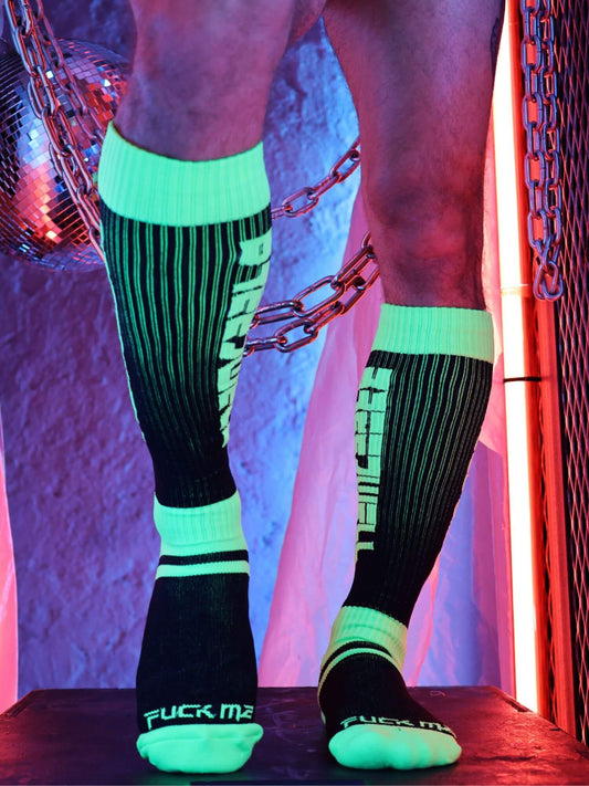 Person wearing black knee-high socks with green accents and visible branding against a colorful background.