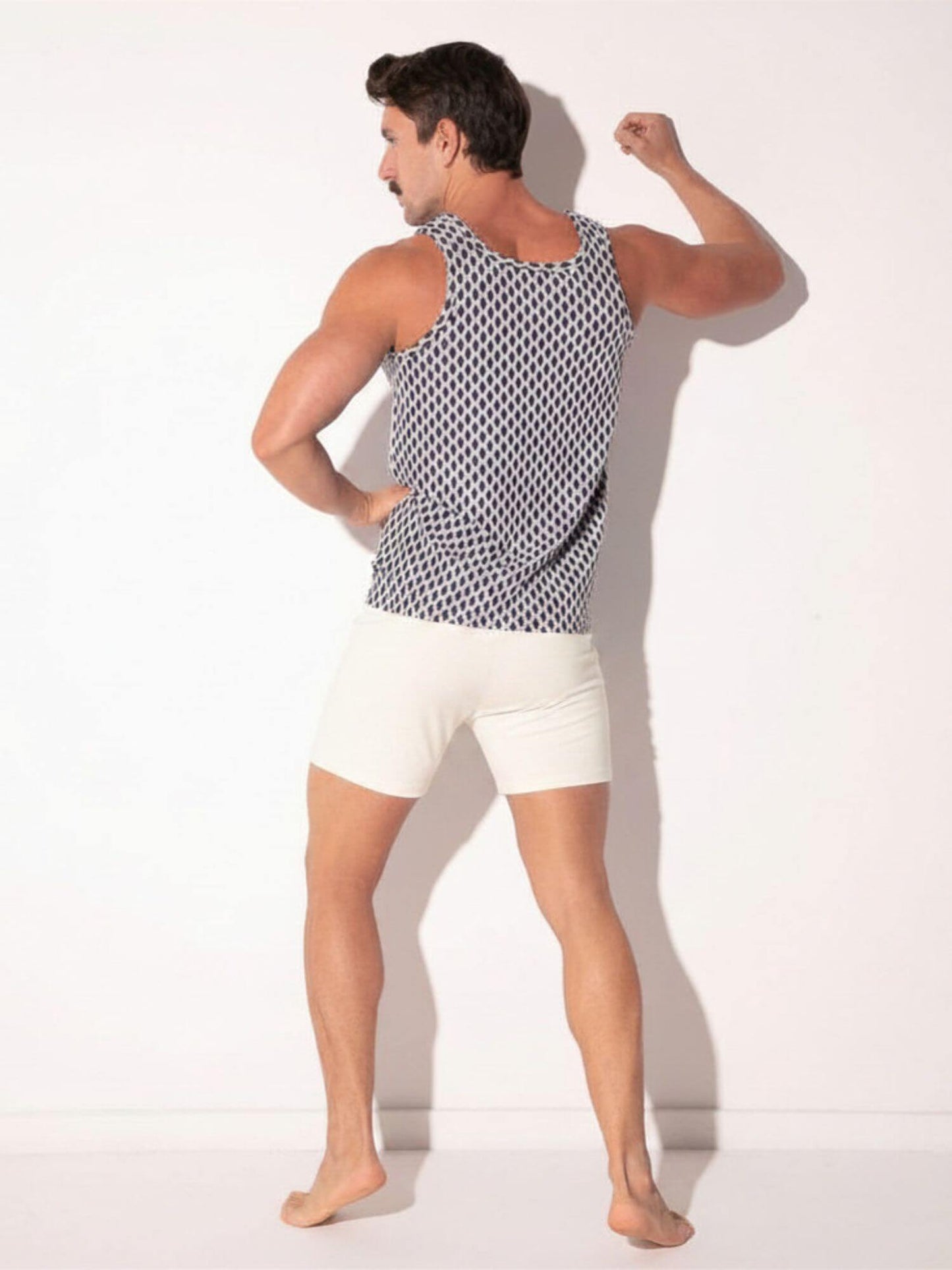 Man wearing a patterned tank top and white shorts on a plain background