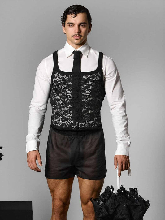 Man wearing a black lace vest over a white shirt with dark shorts, holding a black umbrella on a gray background.