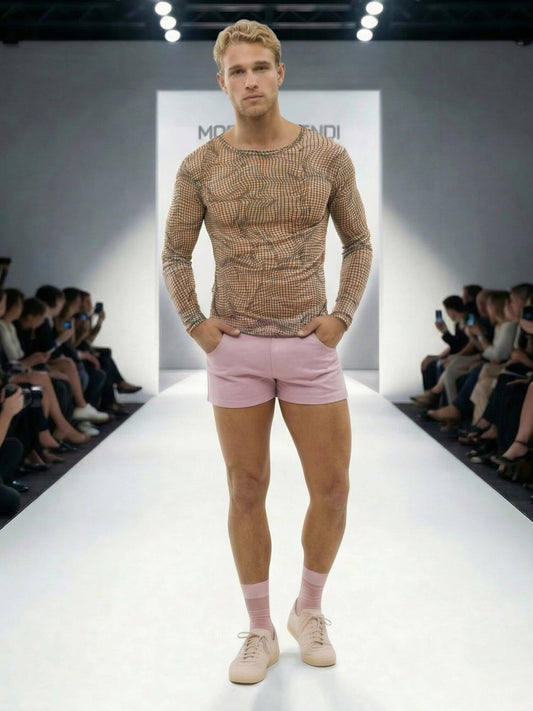 Model walking on a fashion runway wearing a patterned long-sleeve shirt and pink shorts.