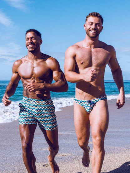 Two men running on a beach wearing patterned swim trunks.