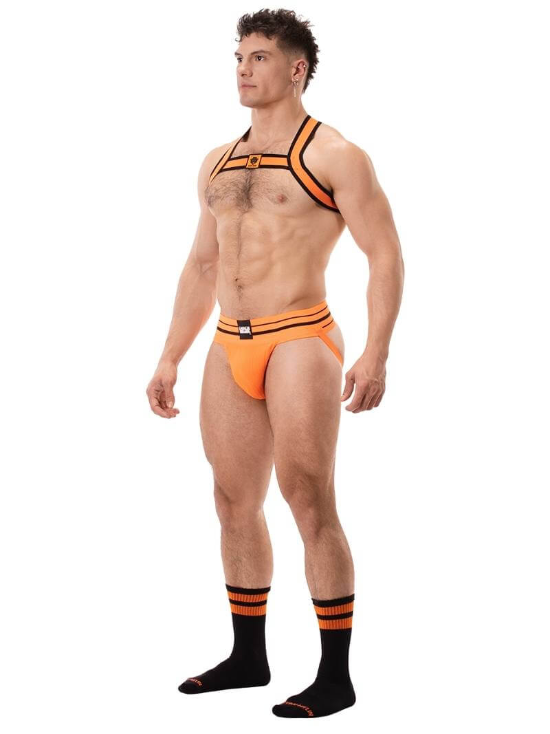 A male model wearing a neon orange and black elastic chest harness with the BARCODE Berlin brand emblem on the front horizontal strap.