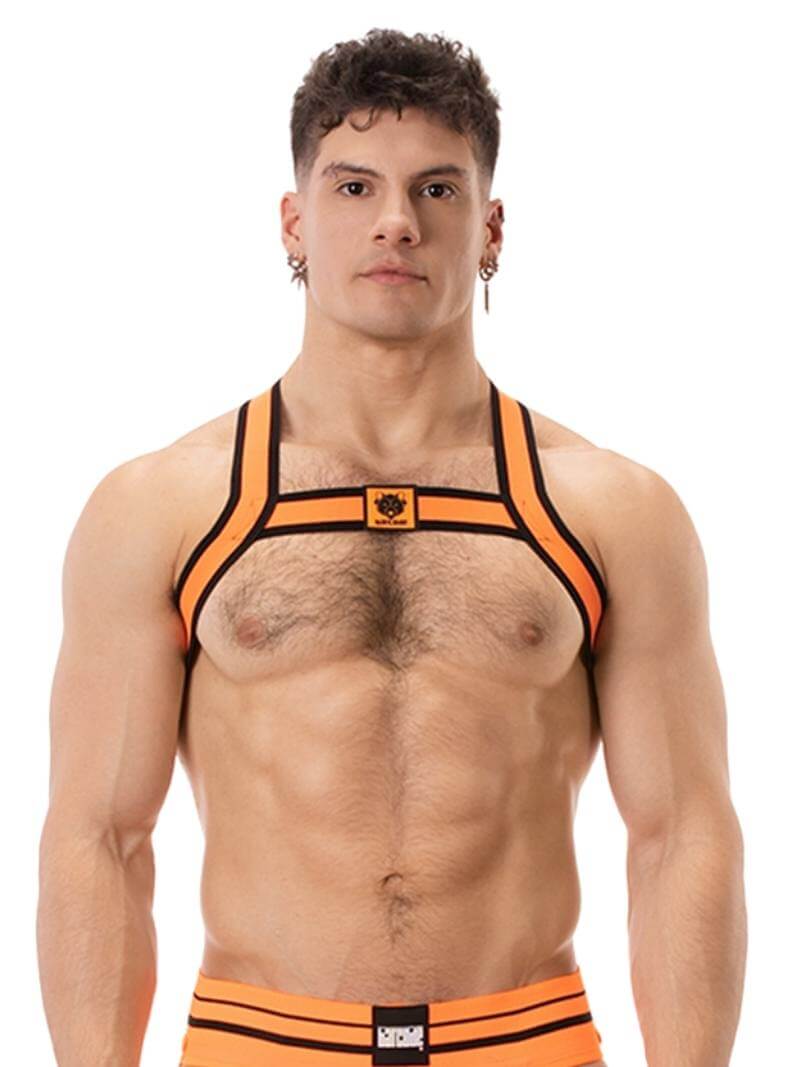 A model wearing an orange and black elastic chest harness with the BARCODE Berlin brand emblem on the front horizontal strap.