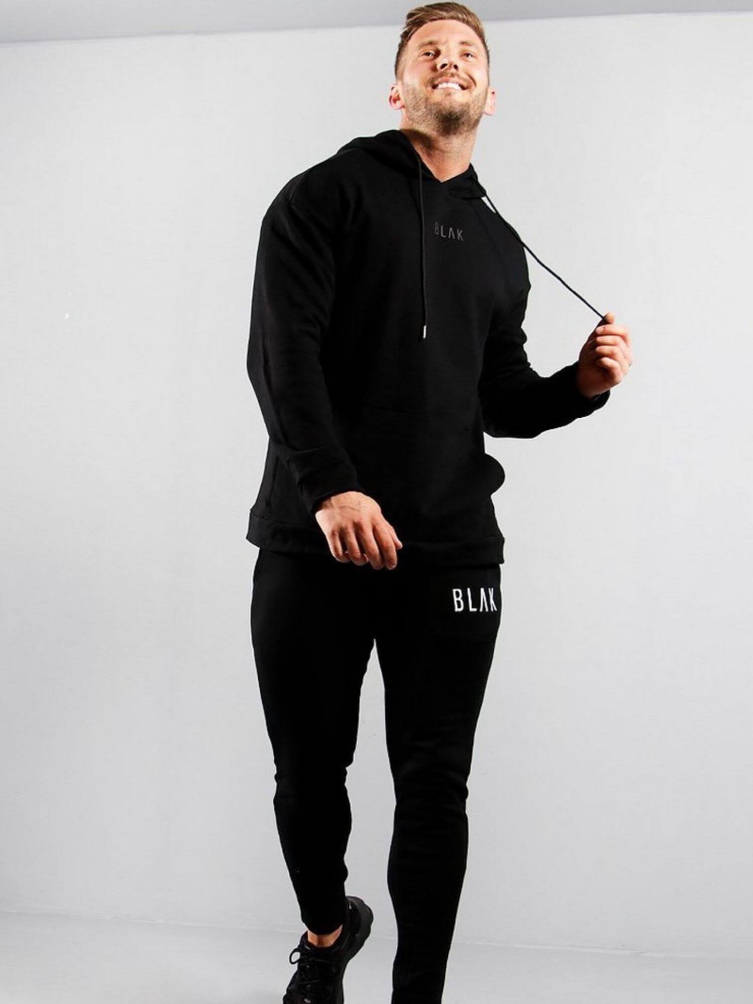 Man wearing a black hoodie and pants with 'BLAK' branding on a white background
