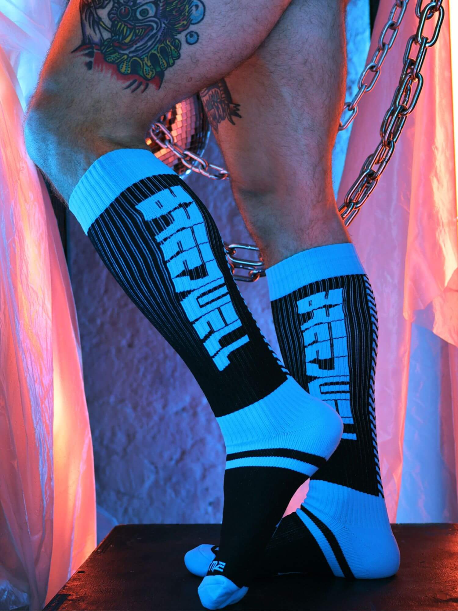 Person wearing black and blue socks with a tattooed arm and chain visible.