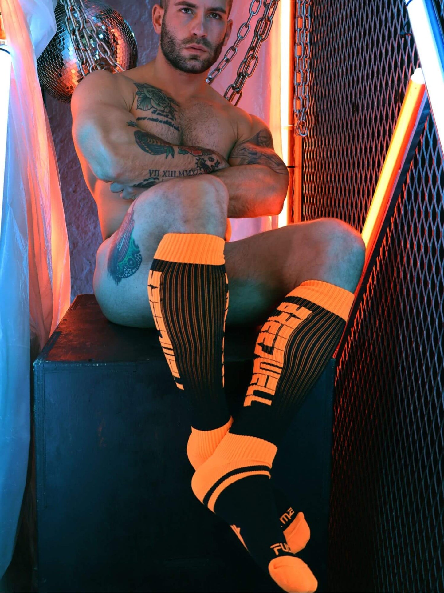 Man wearing black and orange socks with visible branding in a dimly lit room.