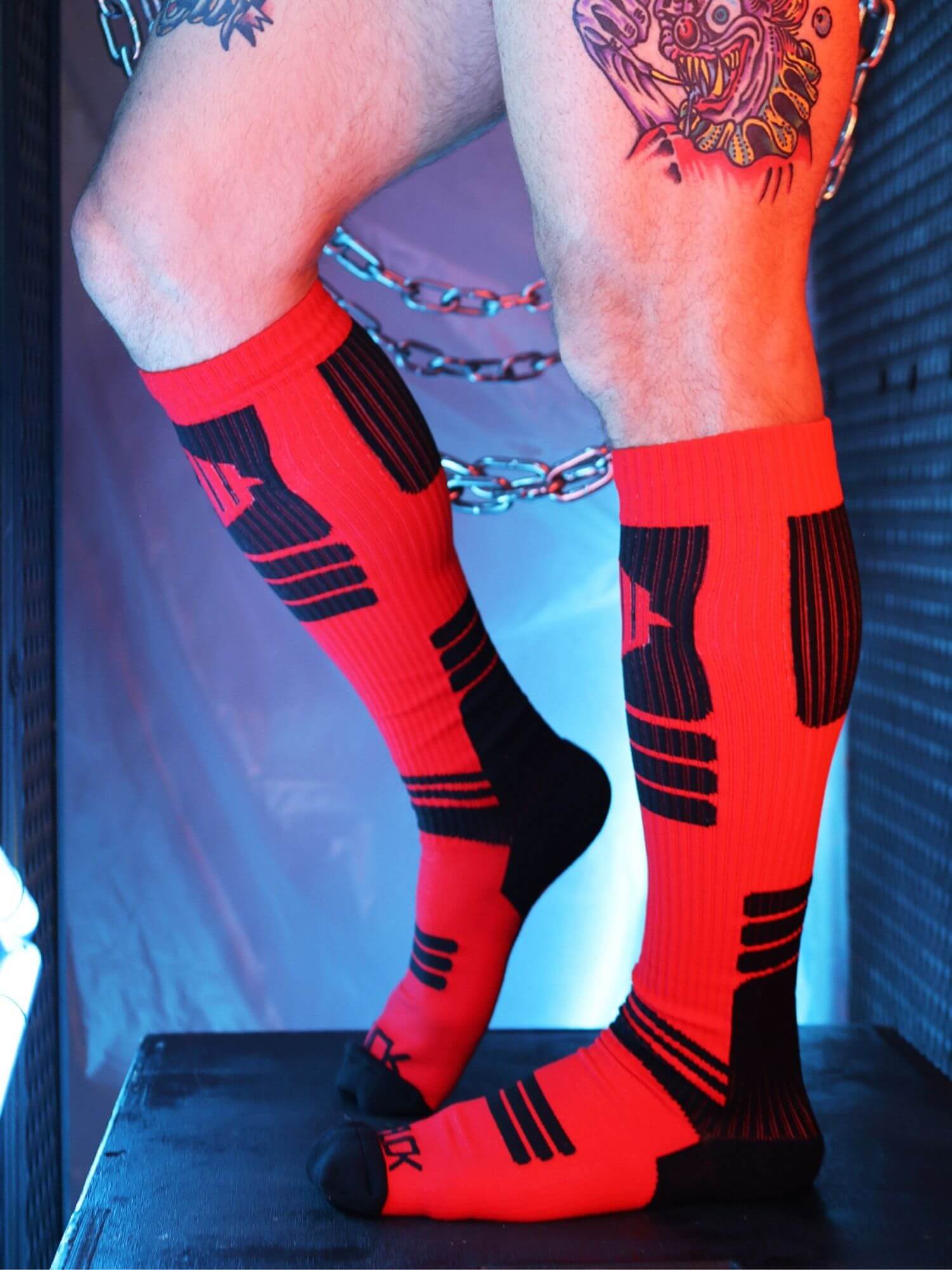 Person wearing red and black knee-high socks with a tattooed arm in the background.