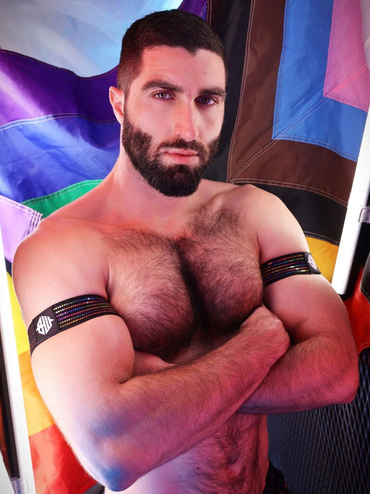 Muscular man with pride armbands on standing in front of a colorful flag