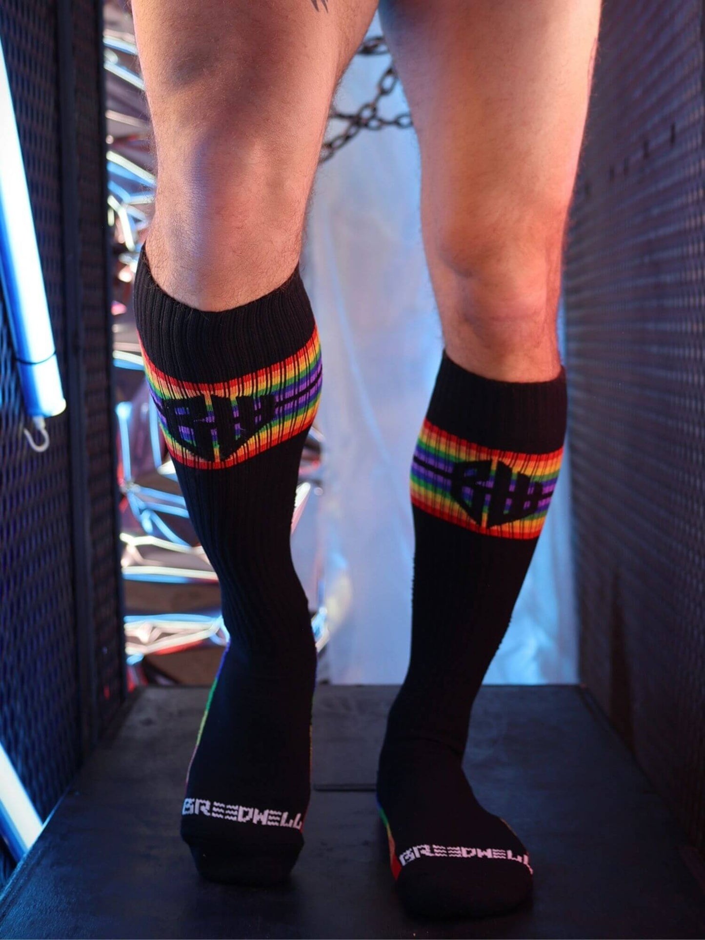 Black knee-high socks with rainbow stripes worn by a person, standing on a dark surface.