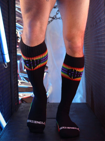 Black knee-high socks with rainbow stripes worn by a person, standing on a dark surface.