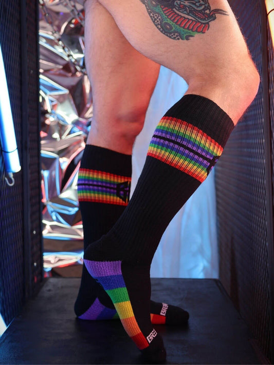 Person wearing black knee-high socks with rainbow stripes in a reflective indoor setting.