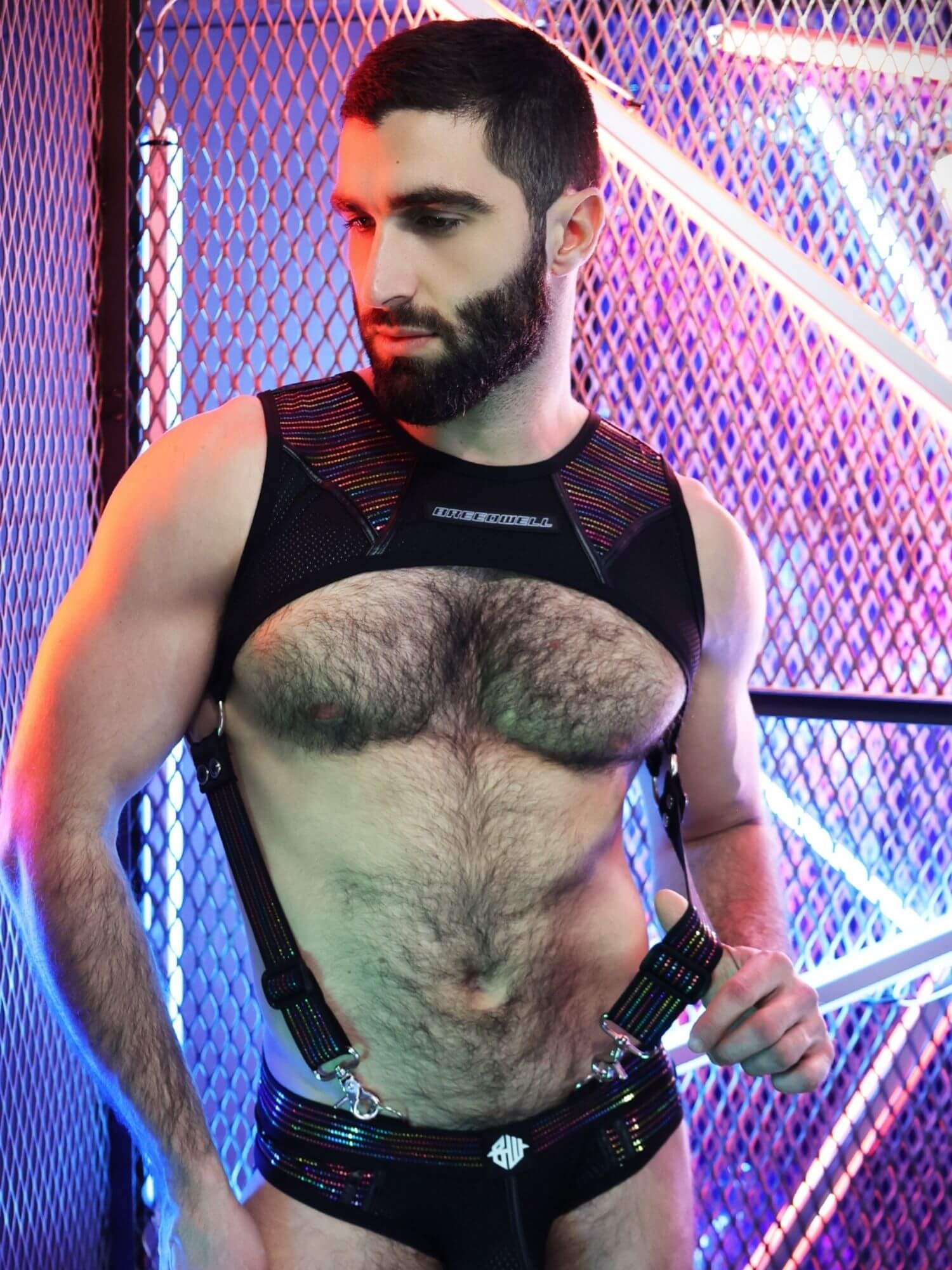 Man wearing a black harness with a metallic sheen against a colorful background