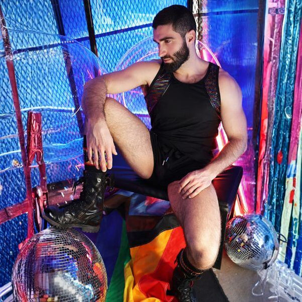 Man in a black tank top and shorts sitting on a colorful rug with disco balls and a vibrant background