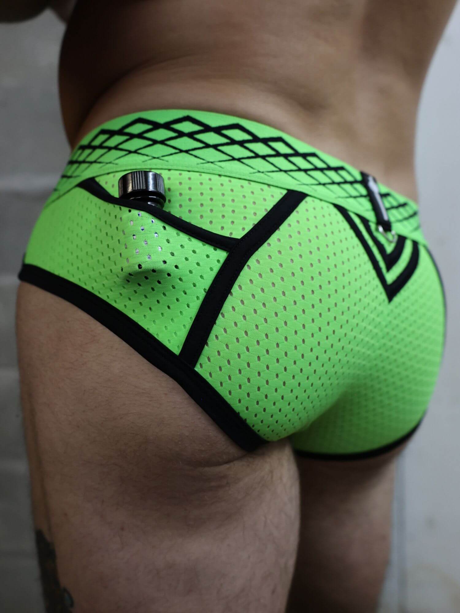 Neon green men's underwear with black mesh and patterns on a neutral background