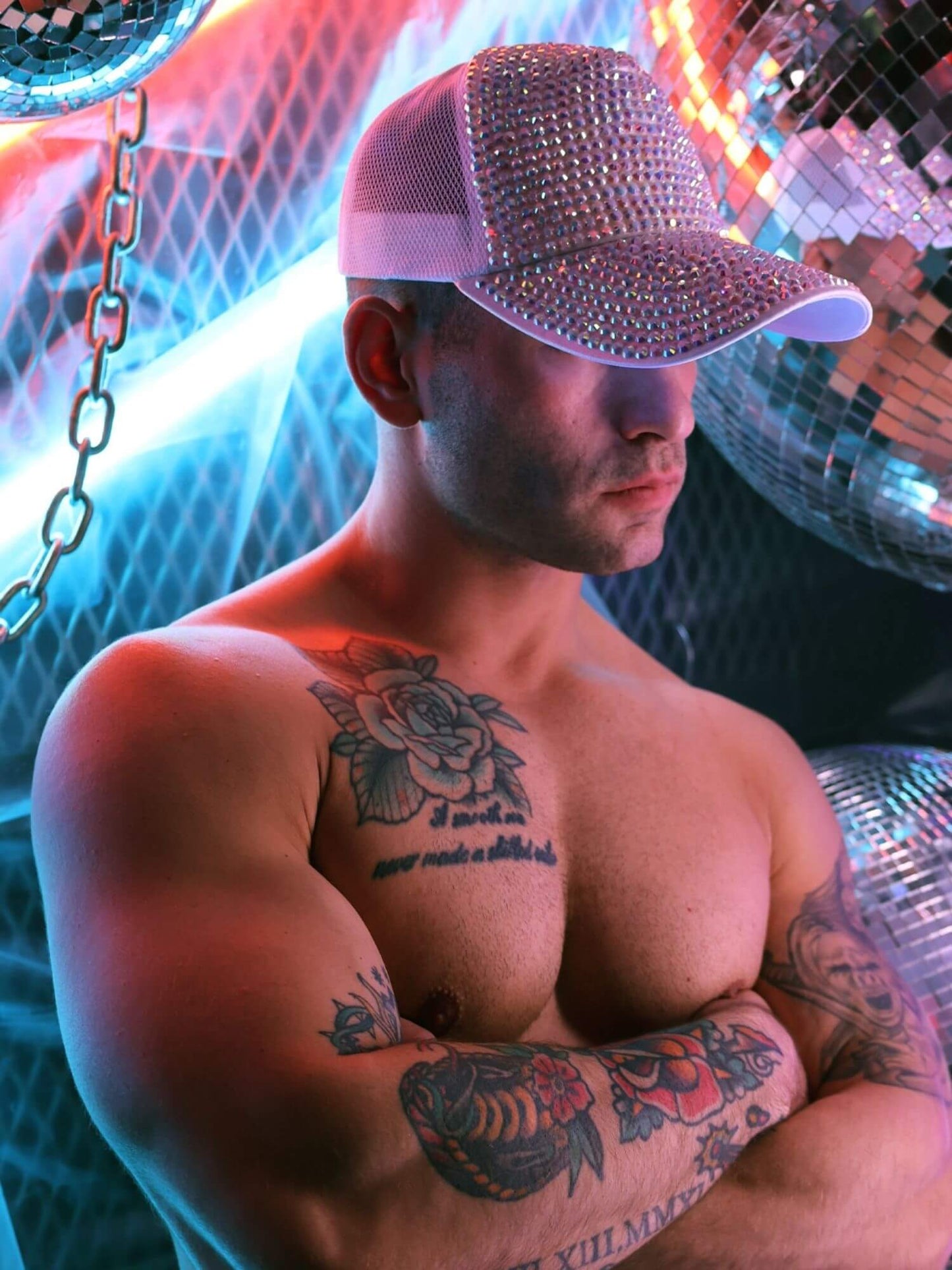 Man wearing a sparkly cap with tattoos in a disco setting