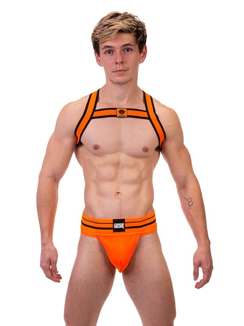 A male model wearing a neon orange and black elastic chest harness with the BARCODE Berlin brand emblem on the front horizontal strap.