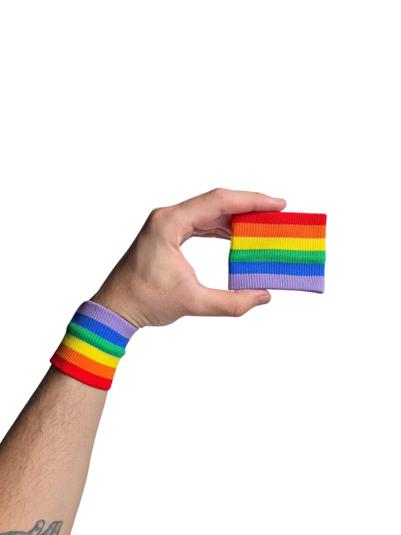 A hand holding two white wristbands with gay pride stripes
