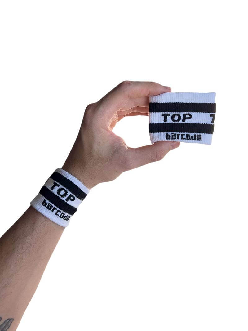 A hand holding two white wristbands with the text 'Top' written in black lettering and a black stripe design.