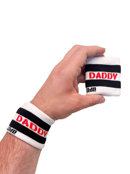 A hand holding two white wristbands with the text 'Daddy' written in black lettering and a black stripe design.
