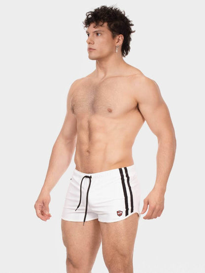 Man wearing white swim shorts with black stripes on a light gray background
