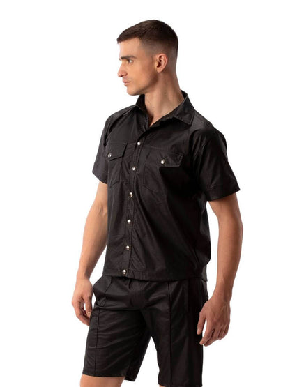 A man wearing a black faux leather shirt with metallic buttons and a collard neck, featuring short sleeves and a buttoned front.