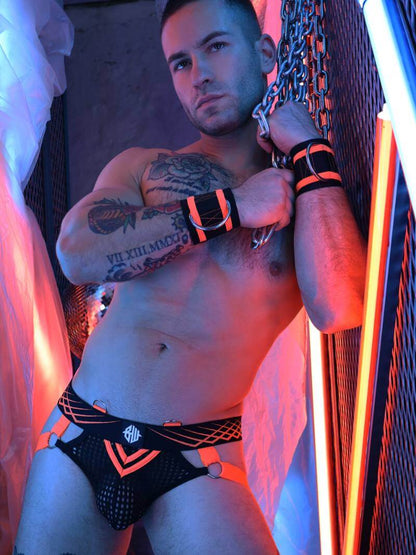 Man wearing black underwear with orange accents in a dimly lit room with neon lights.
