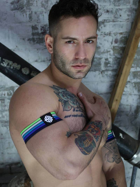 Man with tattoos wearing a black and green armband against a brick wall.
