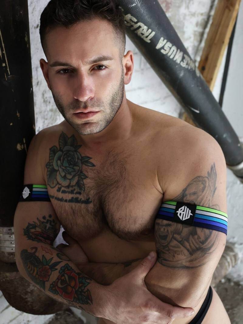 Man with tattoos wearing black arm sleeves with visible branding in an indoor setting.