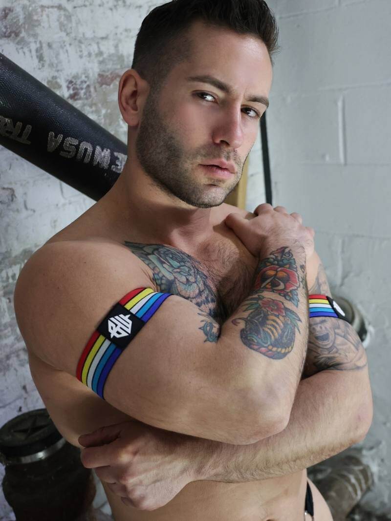 Man with tattoos lifting weights, wearing a rainbow wristband.