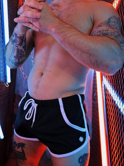 Man wearing black shorts with white drawstrings in a dimly lit room.