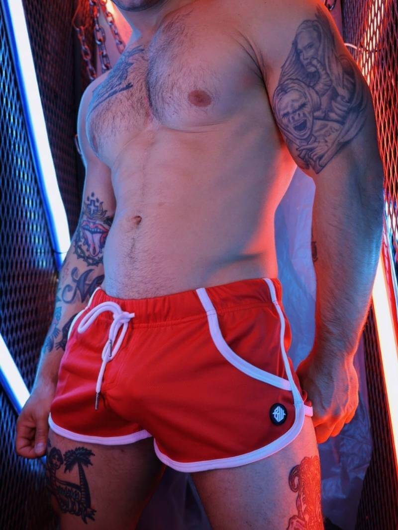 Person wearing red swim shorts with white drawstring and trim, standing against a neon-lit background.