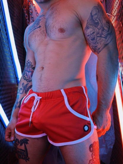 Person wearing red swim shorts with white drawstring and trim, standing against a neon-lit background.