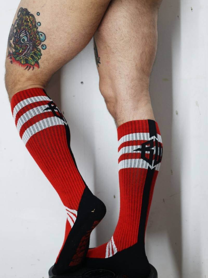 Red and black striped socks worn by a person with tattoos on a white background
