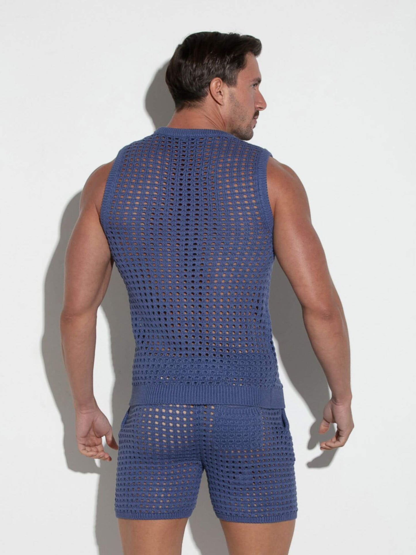Man wearing a blue crochet sleeveless top and shorts against a white background