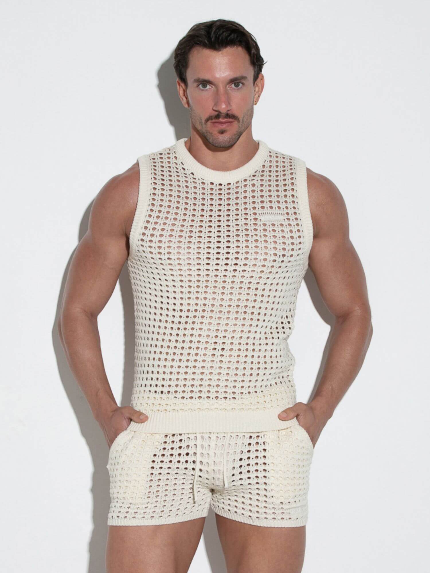 Man wearing a white knitted tank top and shorts set against a plain background