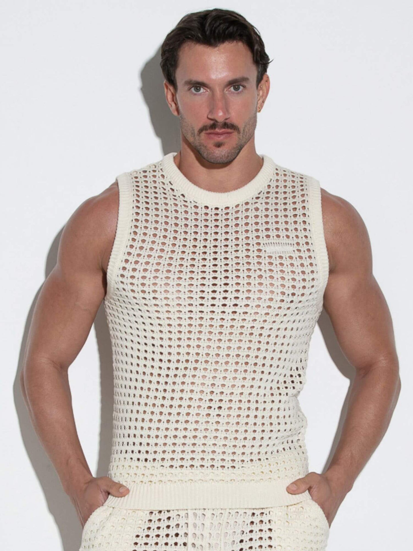 Man wearing a beige sleeveless crochet top against a white background