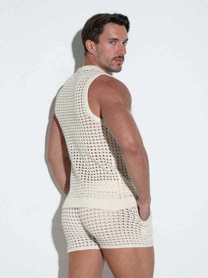 Man wearing a white crochet tank top and shorts against a light background