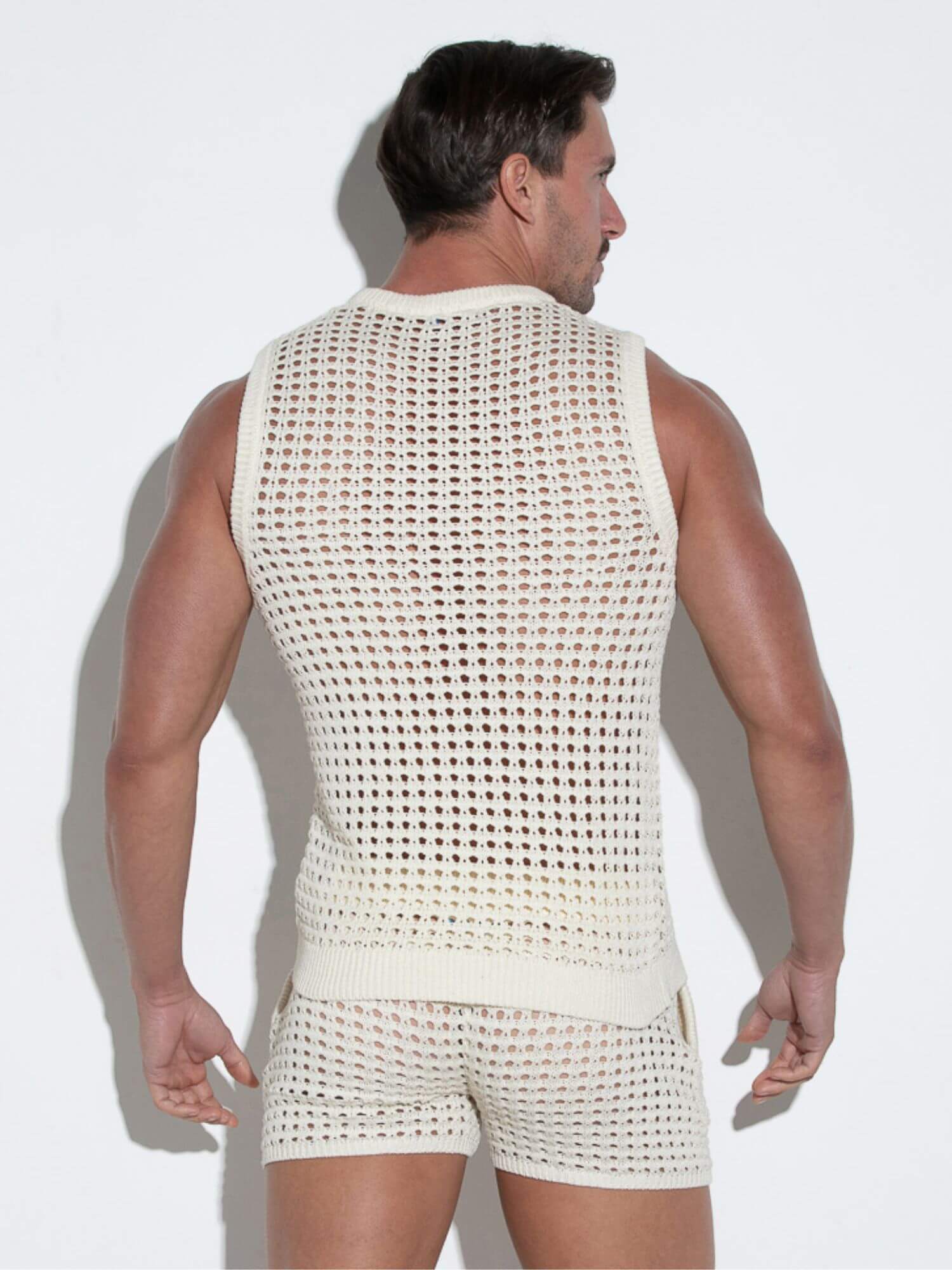 Man wearing a white mesh sleeveless top and shorts against a white background