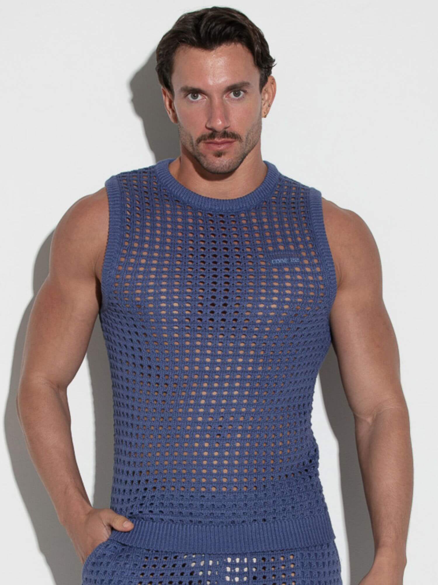 Man wearing a blue sleeveless knit outfit against a white background