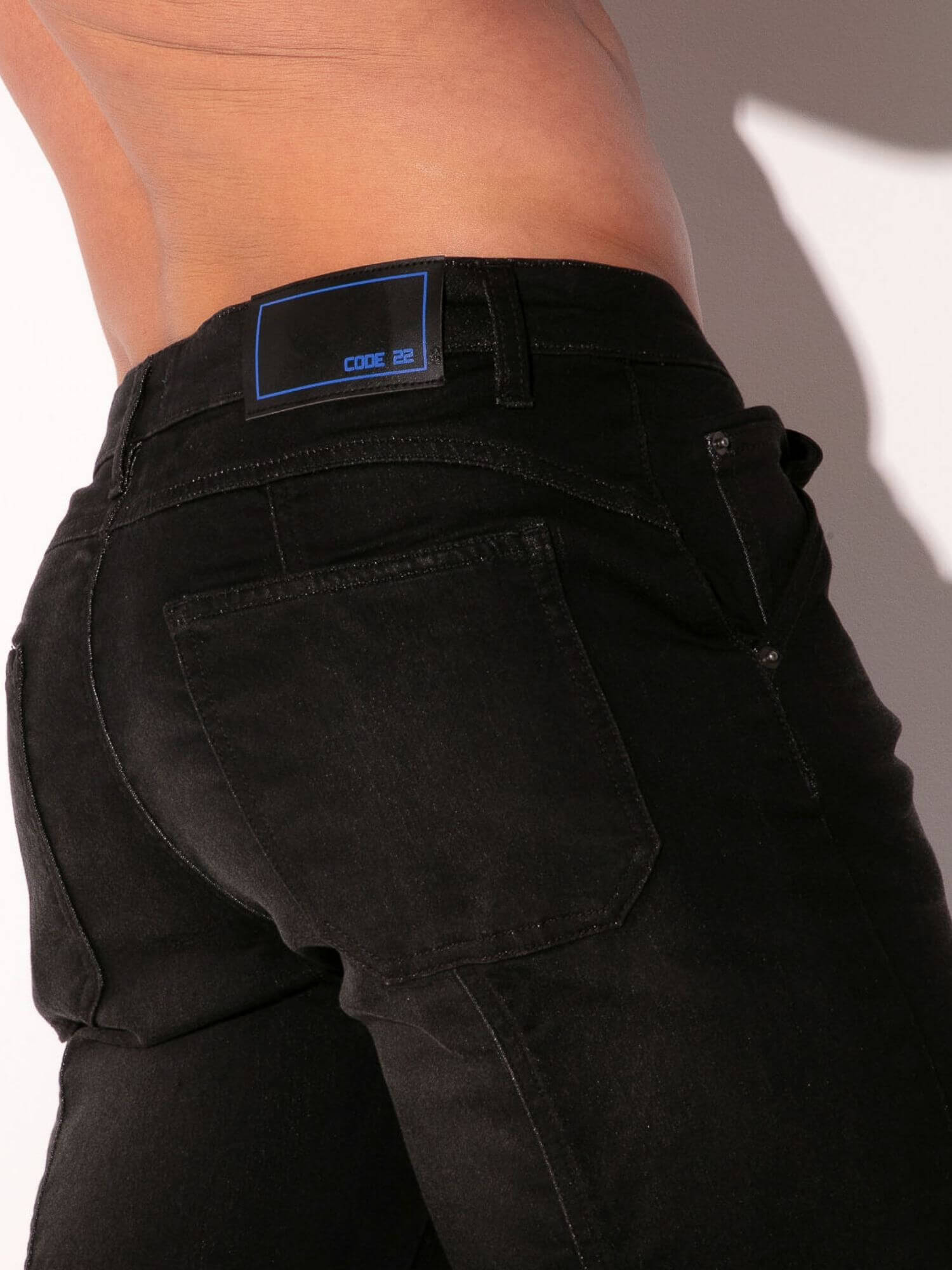 Person wearing black pants with a visible brand label on the back pocket against a neutral background