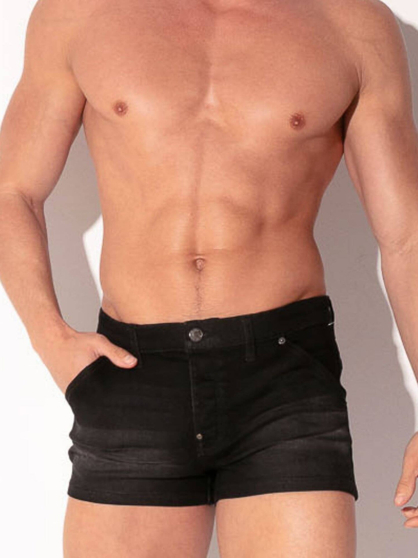 Man wearing black denim shorts against a neutral background