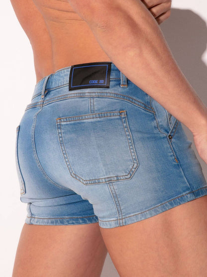 Person wearing blue denim shorts with a visible brand label on a plain background