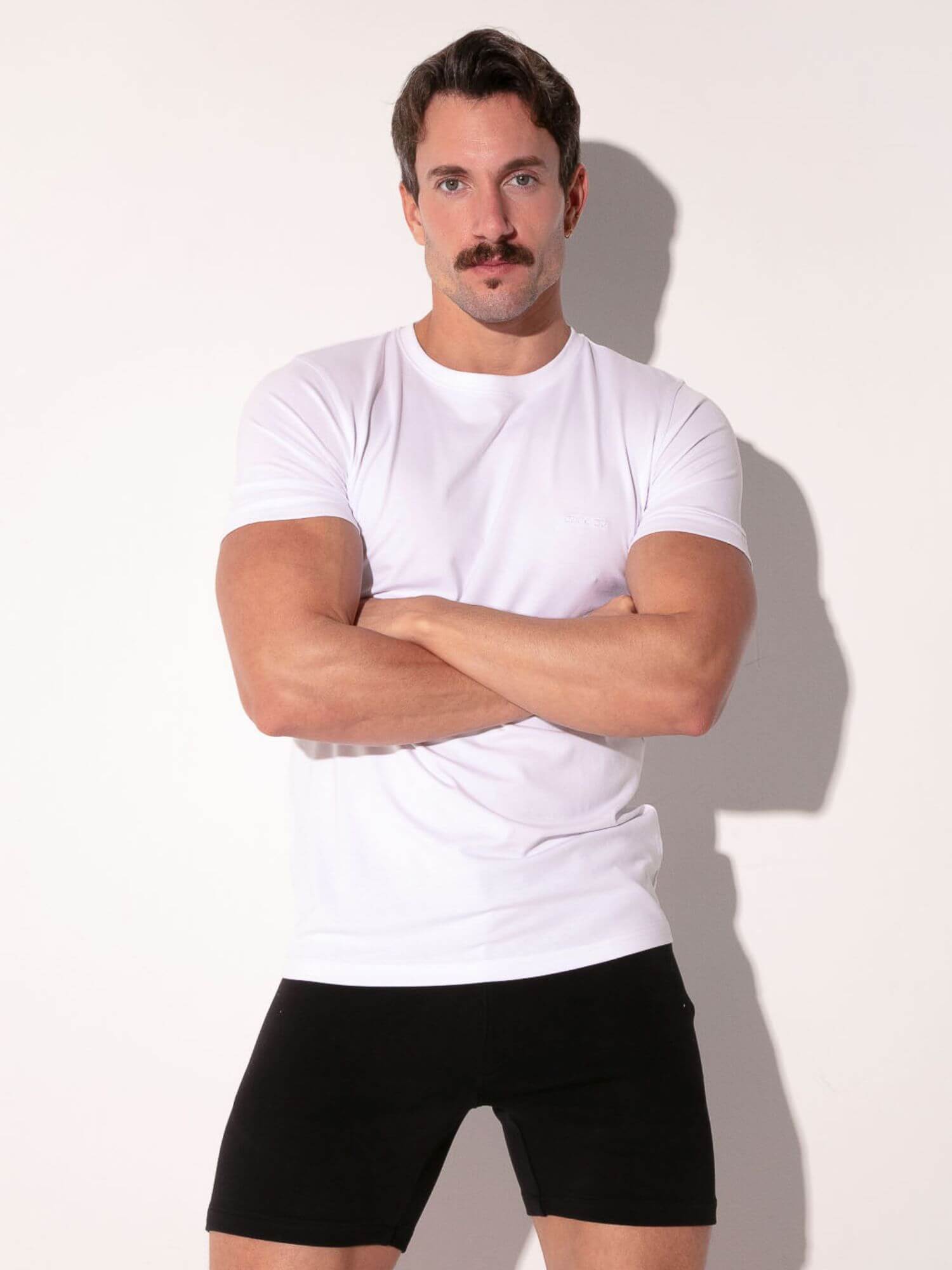 Man wearing a white t-shirt and black underwear against a plain background