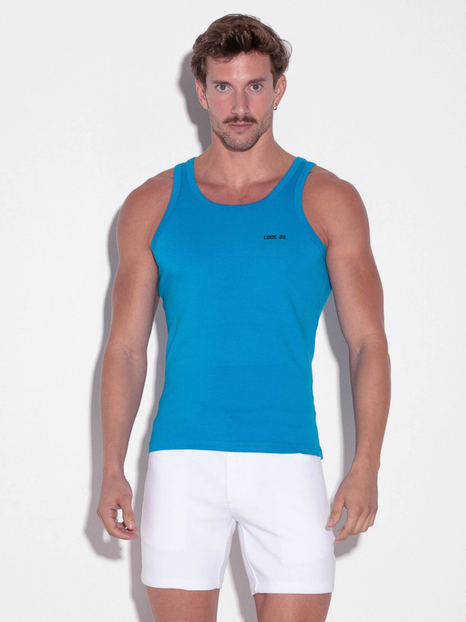 Man wearing a blue tank top and white shorts on a light background