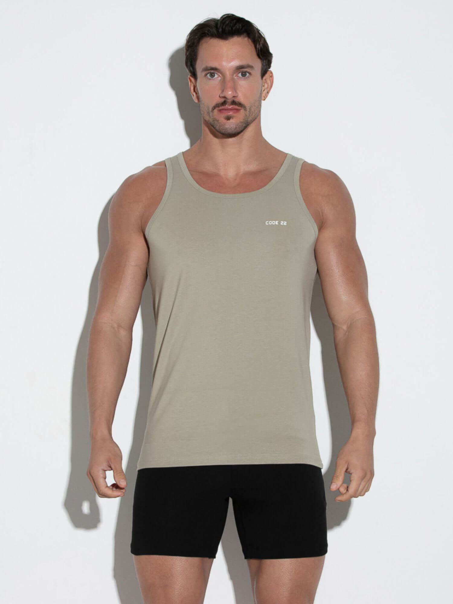 Man wearing a beige tank top and black shorts against a white background