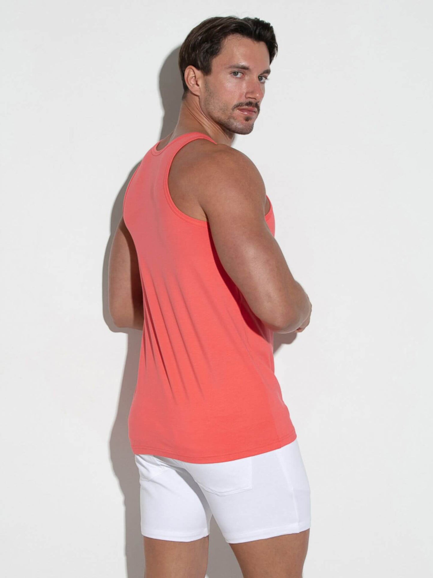 Man wearing a coral tank top and white shorts against a light background