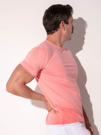 Man wearing a pink t-shirt and white pants against a plain background