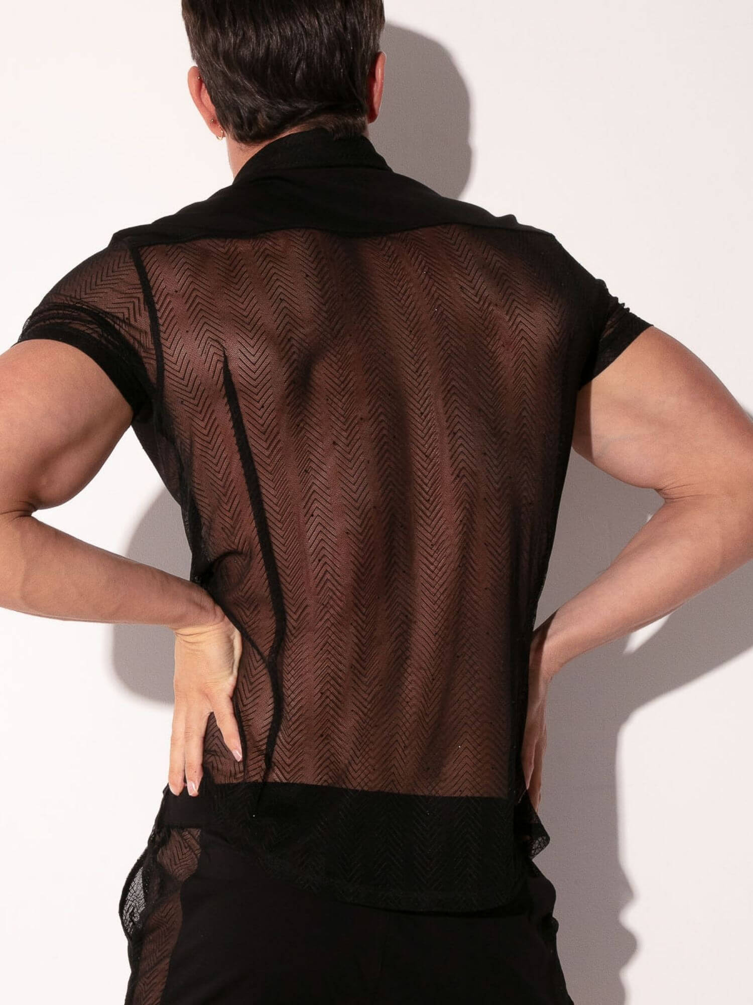 Person wearing a sheer black top with a plain background