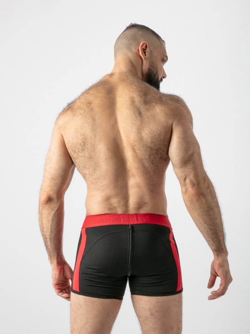 Man wearing black swim shorts with red side panels on a white background